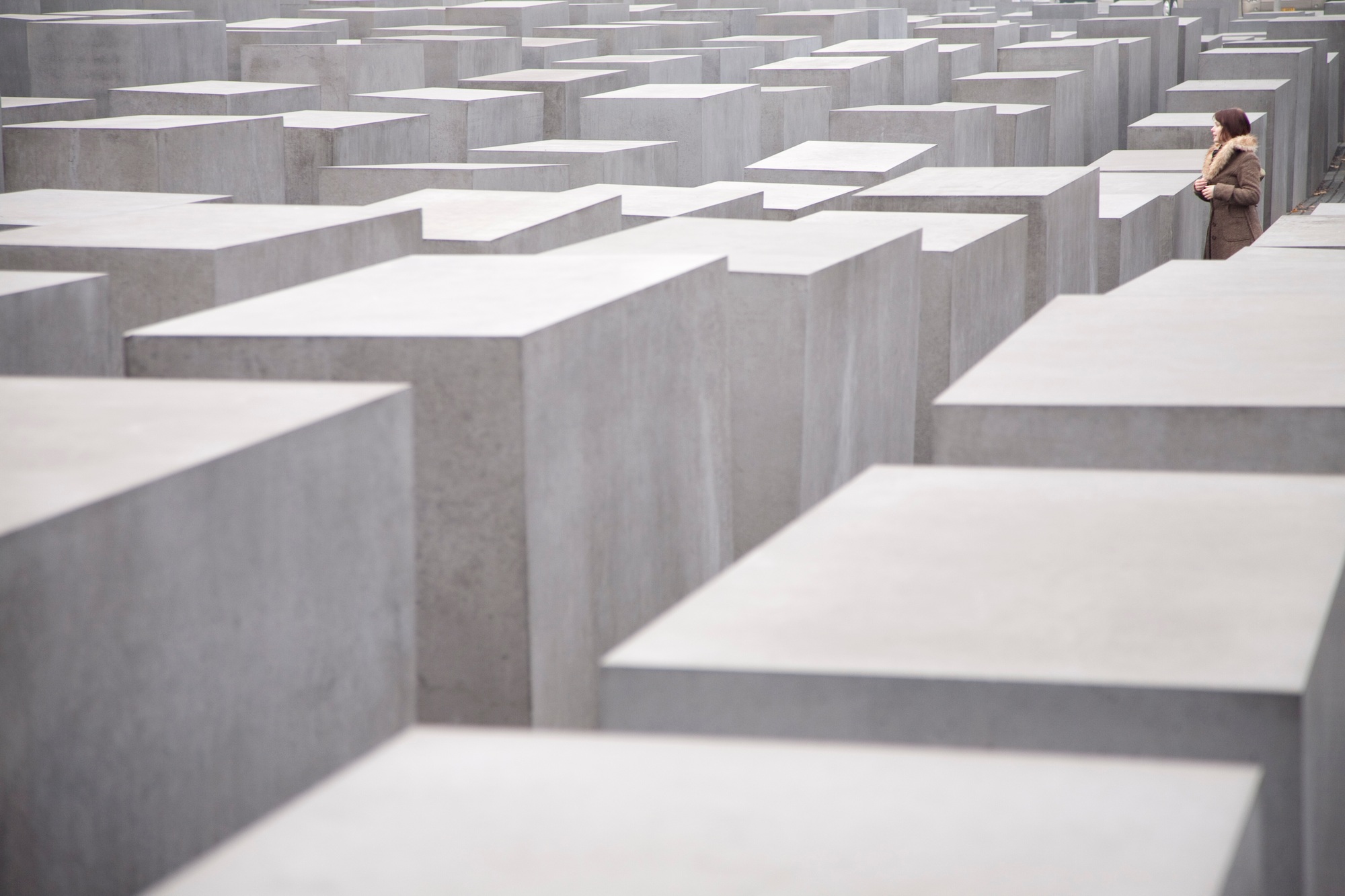A solitary figure lost in thought among a maze of somber blocks.